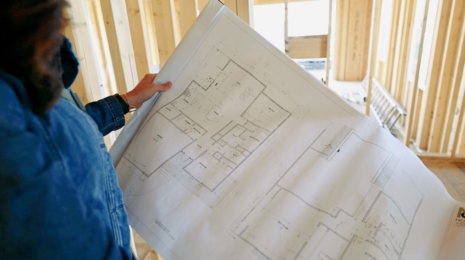 picture of a woman looking over the blueprints of a home build with the framing visible in the background