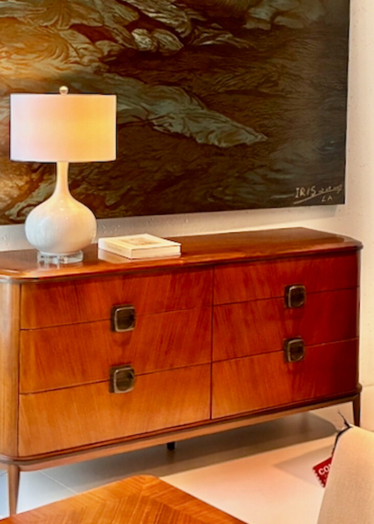 Mid century style wooden dresser sitting beneath a painting with a mid-century modern ceramic onion table lamp on top.
